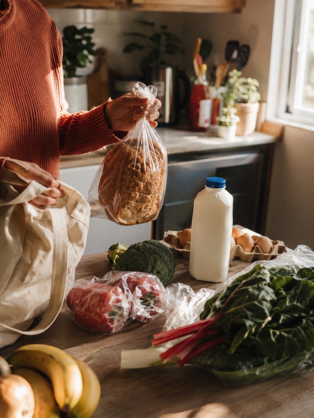 Someone unpacking groceries in a kitchen: bread, milk, eggs and greens on the counter