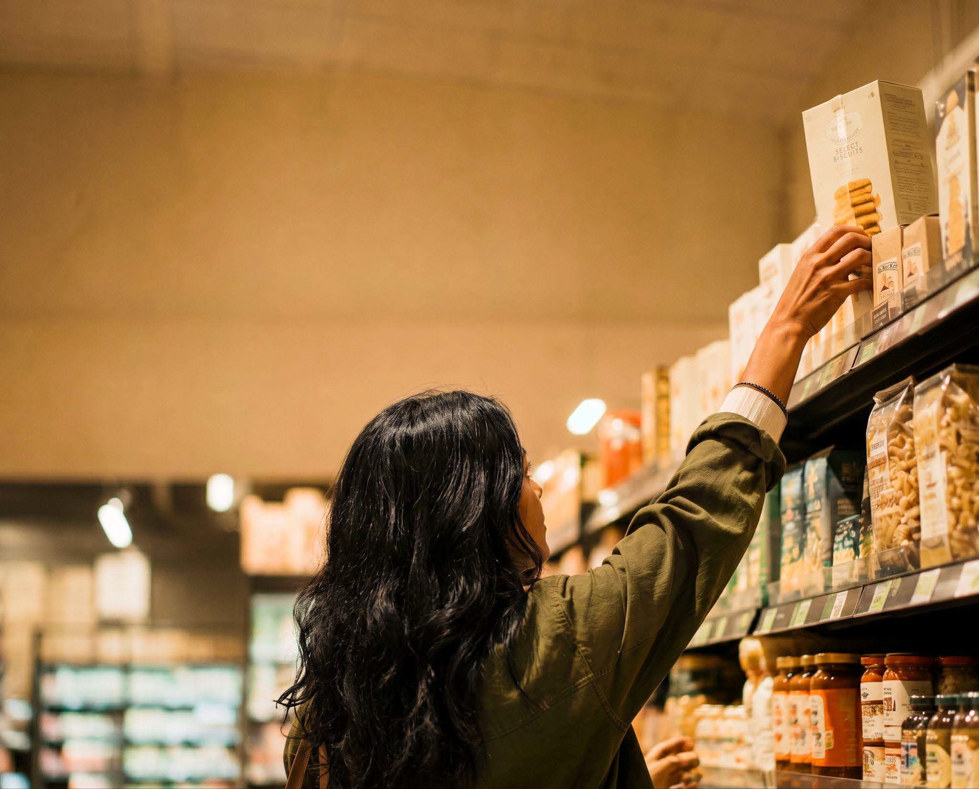 A woman reaching for an item on a supermarket shelf